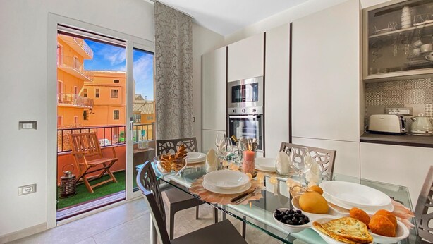 Una cucina moderna con tavolo da pranzo in vetro, elettrodomestici in acciaio inossidabile e un balcone vista edifici.