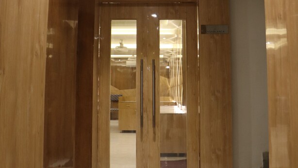 A wooden door with a glass panel and a nameplate, leading to a room with a tiled floor. - Signum CityScapes The Royal Castle Plaza (Rajkot)
