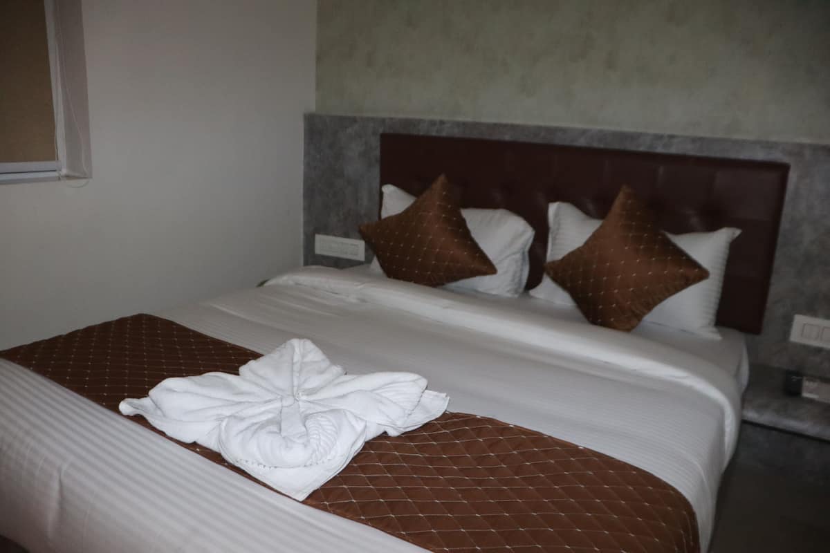 Una cama bien tendida con una colcha acolchada marrón y ropa de cama blanca, incluyendo una toalla doblada sobre la cama.