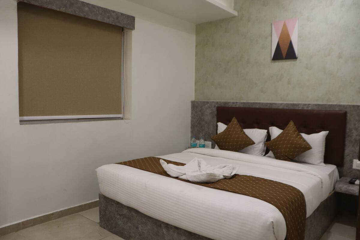 Habitación de hotel con una cama, ventana con cortina, una obra de arte en la pared y una mesita de noche con lámpara.