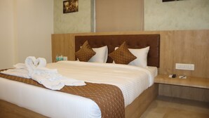 A hotel room with a large bed, a wooden headboard, and a nightstand with a phone and remote control. - Signum CityScapes The Royal Castle Plaza (Rajkot)