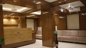 A reception area with a wooden reception desk, a sofa, and a potted plant. - Signum CityScapes The Royal Castle Plaza (Rajkot)