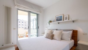 A bedroom with a bed, a window with curtains, a balcony, and a shelf with pictures. - Gran Torino 17 in Cattolica (Cattolica)