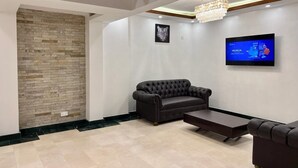 A modern living room with a stone accent wall, a black leather sofa, a wooden coffee table, and a flat-screen TV mounted on the wall. - Dune View Hotel (Mombasa)