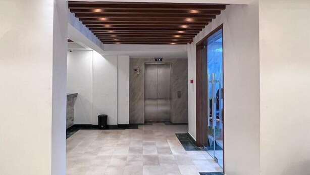 A modern interior with a checkered floor, a central elevator, and a wooden ceiling with recessed lighting. - Dune View Hotel (Mombasa)