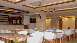 A restaurant with white chairs and tables, wooden beams on the ceiling, and a stone pillar. - Dune View Hotel (Mombasa)