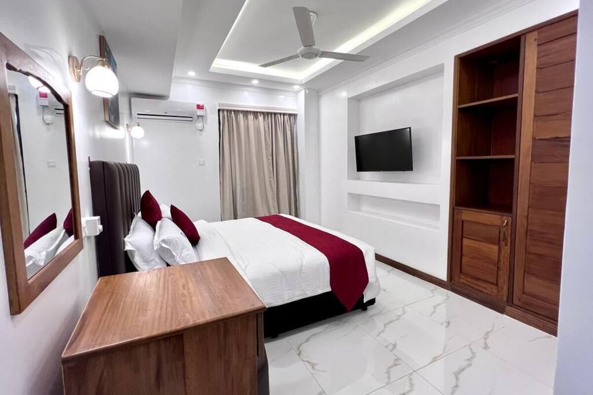 A hotel room with a bed, a desk, a TV mounted on the wall, and a wardrobe.