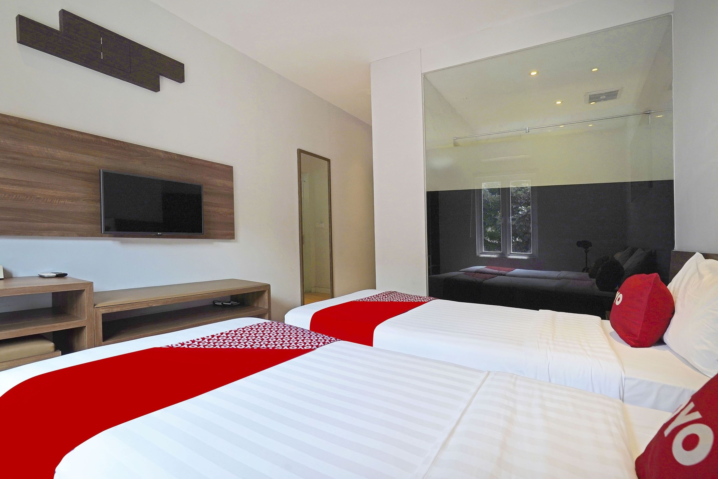 A hotel room with two beds, a TV mounted on the wall, a wooden console table, and a large window.