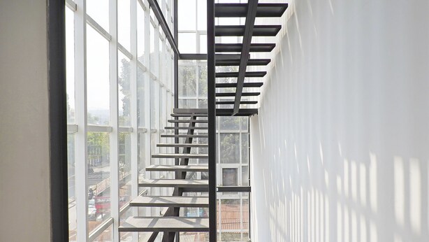 Ein modernes Interieur mit einer Treppe zu einem Balkon, großen Fenstern und Außenblick.