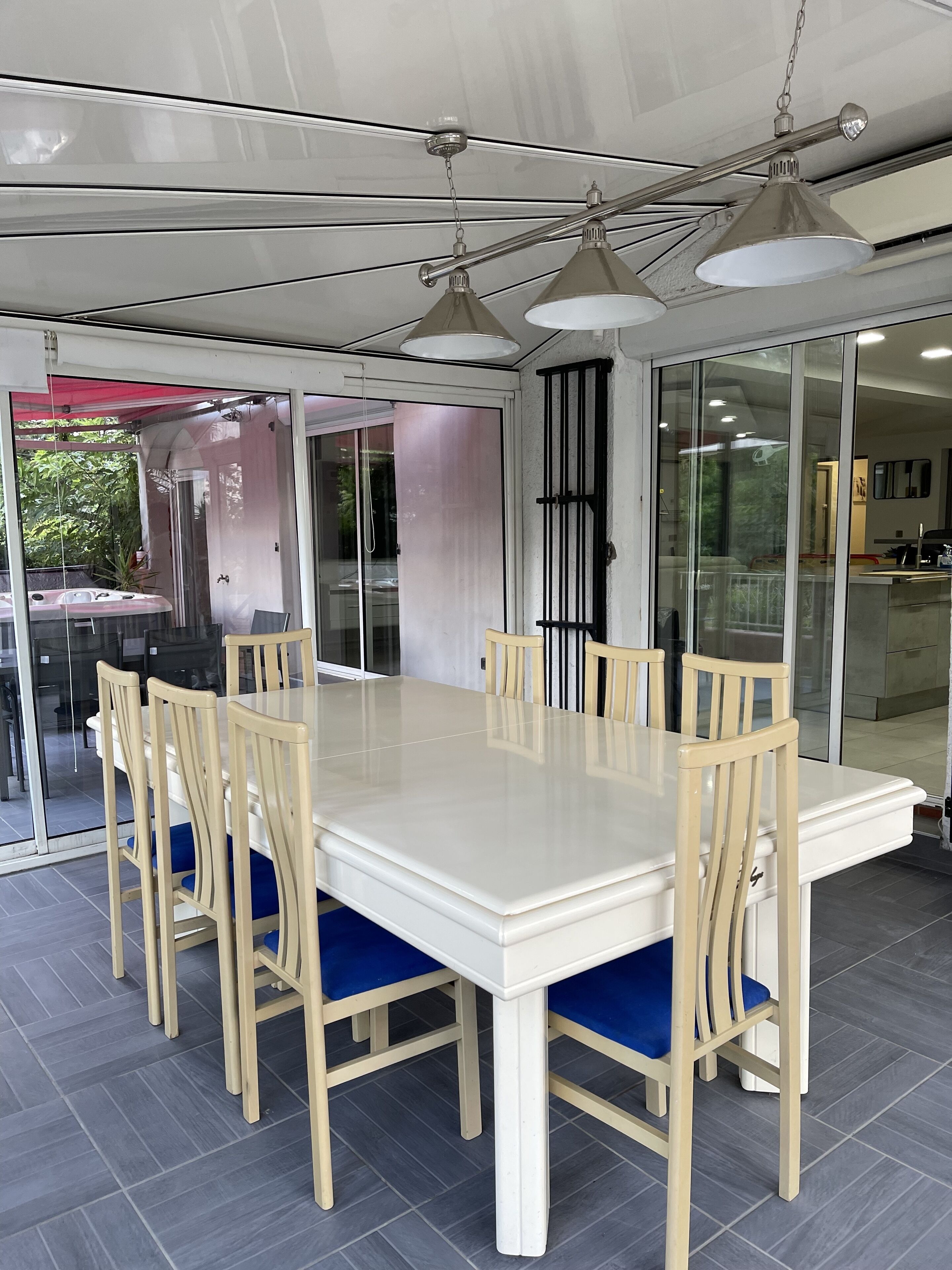 A spacious dining area with a large white table and wooden chairs with blue cushions.
