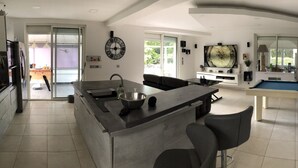 Een moderne keuken met een centraal eiland, een eethoek met een pooltafel, en een woonkamer met een grote televisie.