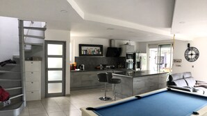 Una sala de estar moderna con mesa de billar, una zona de cocina y una escalera.
