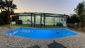Una piscina con cerramiento de vidrio, baldosas de piedra y sillas de descanso.