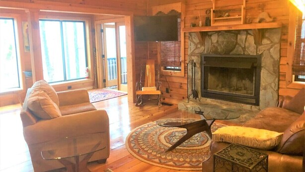 A cozy log cabin interior with a fireplace, leather sofas, and a large window. - Little Bushy Head -Blue Ridge cabin rental- Wifi- (Blue Ridge)