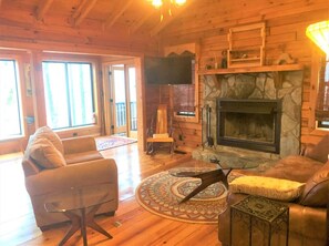 A cozy log cabin interior with a fireplace, leather sofas, and a large window.