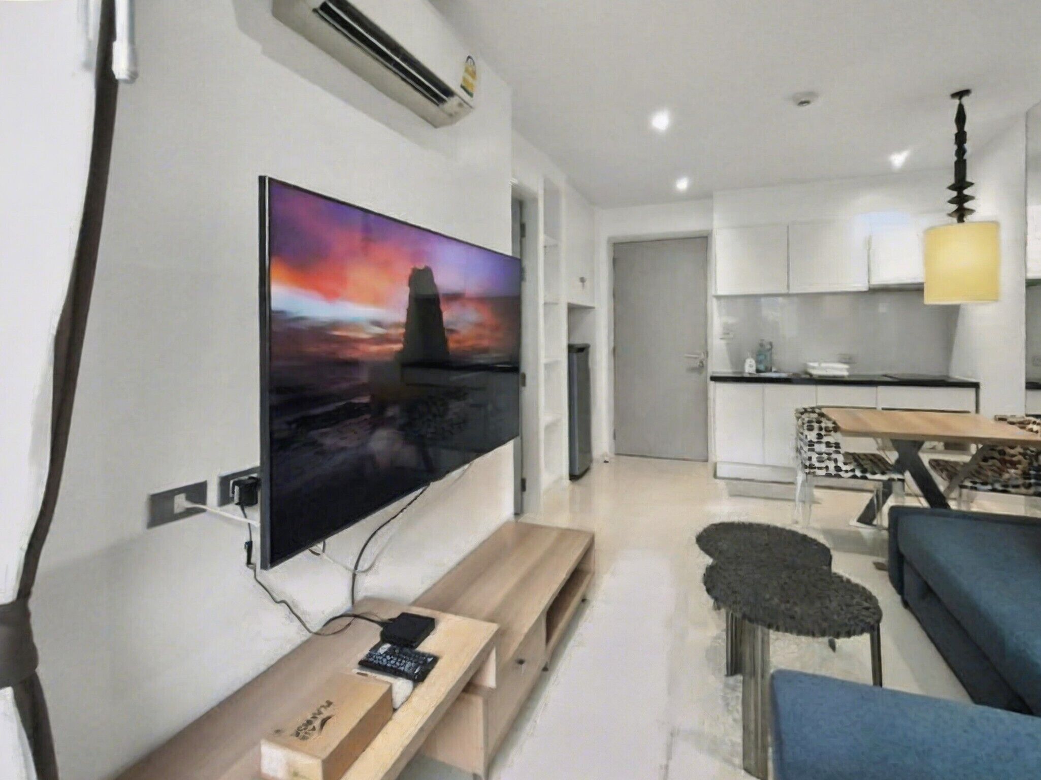 A modern living room with a flat-screen TV, a wooden bench, a sofa, and a dining area with a table and chairs.