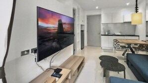 Una sala de estar moderna con un televisor de pantalla plana, un banco de madera, un sofá y un comedor con una mesa y sillas.
