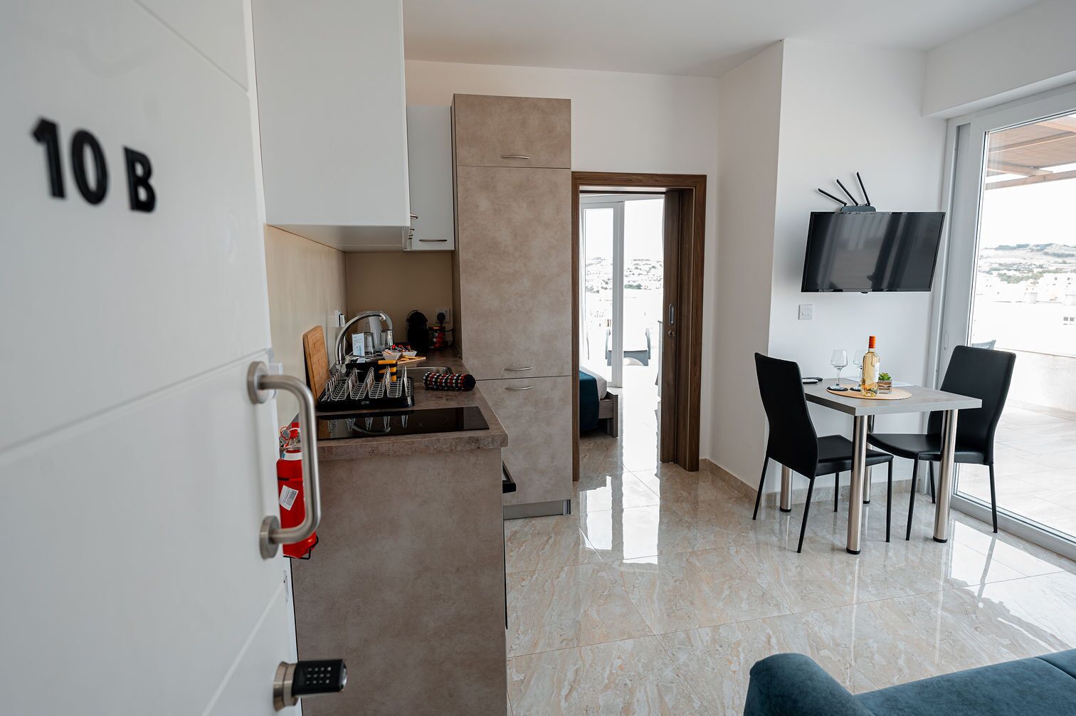A modern hotel room with a kitchenette, a dining area, and a TV mounted on the wall.