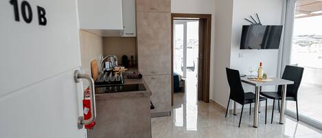 A modern hotel room with a kitchenette, a dining area, and a TV mounted on the wall.