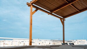 Un bain à remous sous une pergola en bois, avec vue sur une plage et des bâtiments en arrière-plan.