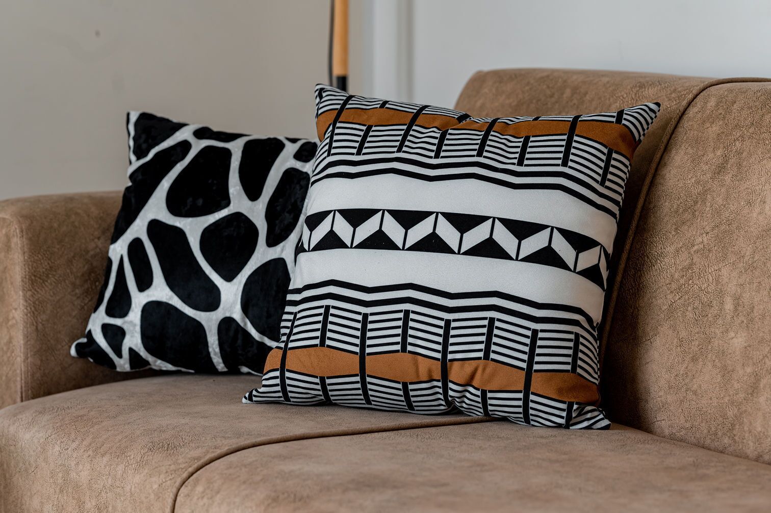 Un divano color beige con due cuscini decorativi, uno con motivo astratto in bianco e nero e l'altro con un design geometrico.