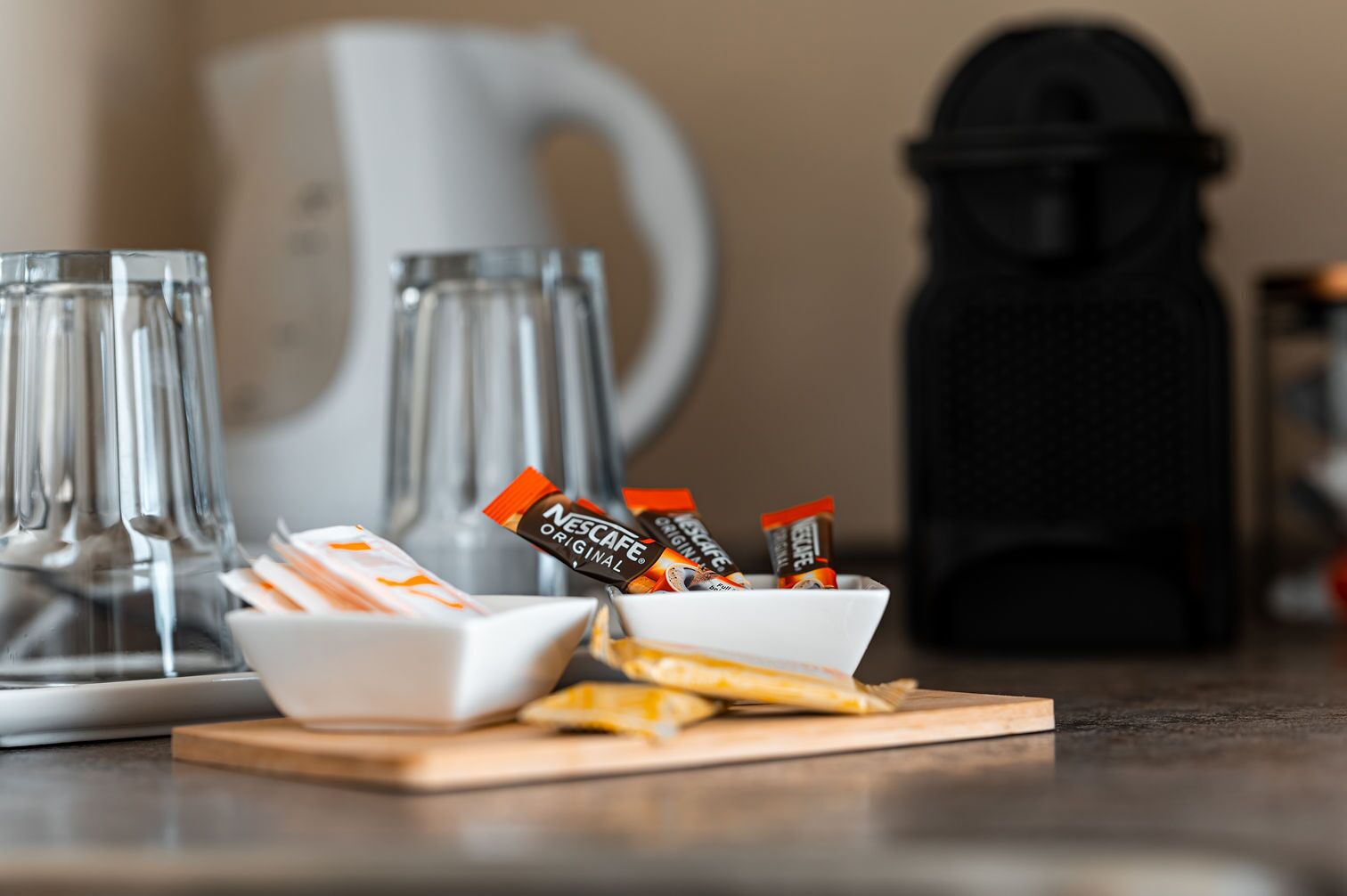Una encimera de cocina con una cafetera, un hervidor y una caja de café instantáneo Nescafé Original.