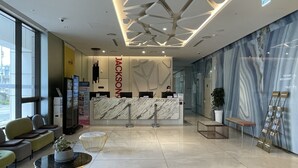A modern hotel reception area with a marble reception desk, seating arrangements, and directional signage for amenities. - Jackson9s Hotel (Chuncheon)