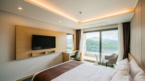 A modern hotel room with a large bed, a flat-screen TV mounted on the wall, a desk with a chair, and a balcony with a view of the mountains. - Jackson9s Hotel (Chuncheon)
