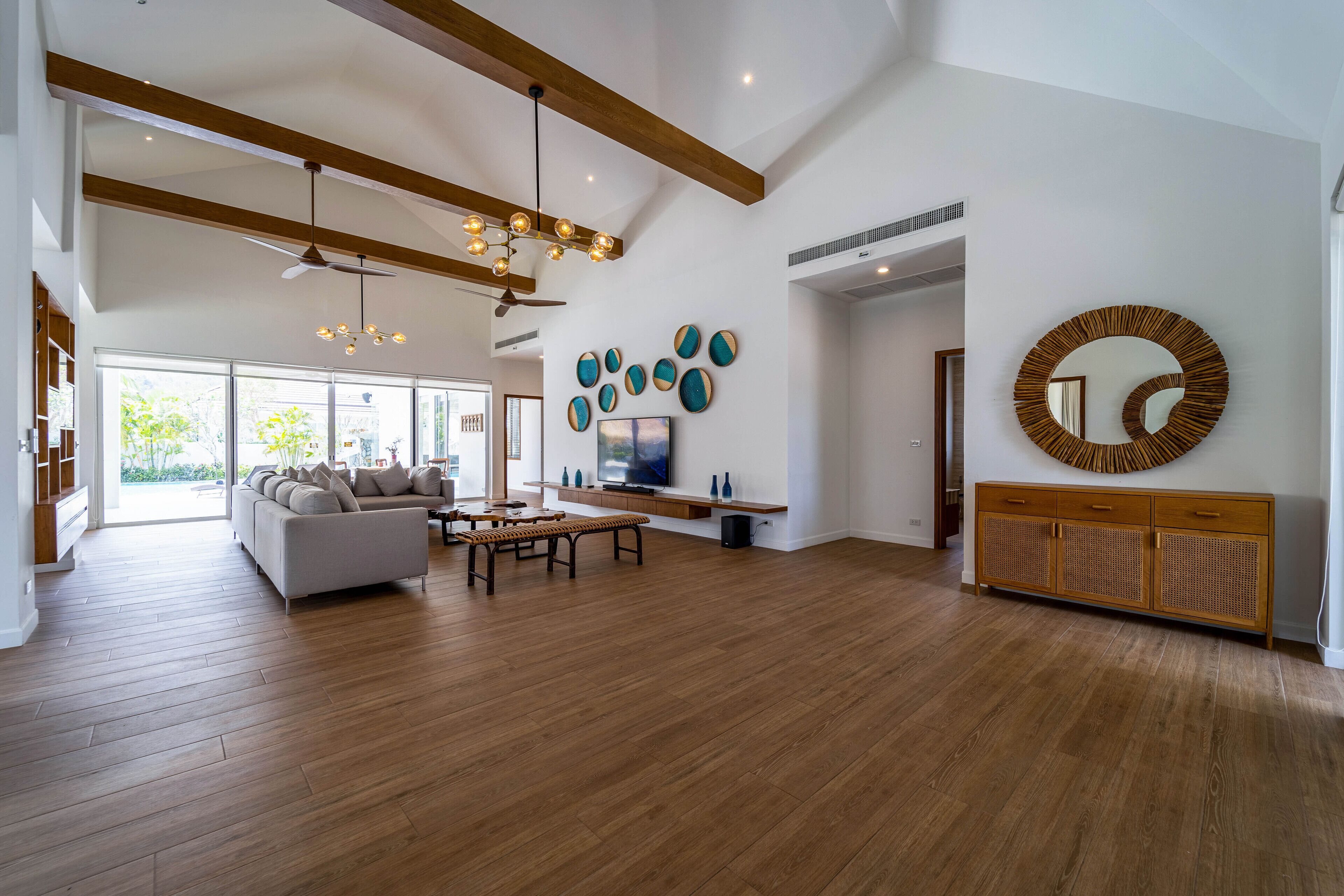 A spacious living room with a large sofa, wooden flooring, a dining table, and a TV.
