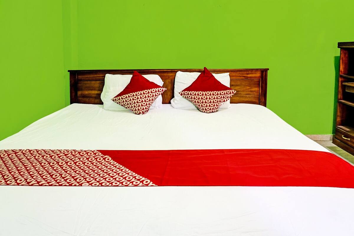 Una cama con cabecera de madera, dos almohadas rojas y una colcha blanca.