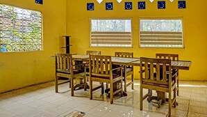 A dining area with a yellow wall, a large window with blinds, and a patterned floor.
