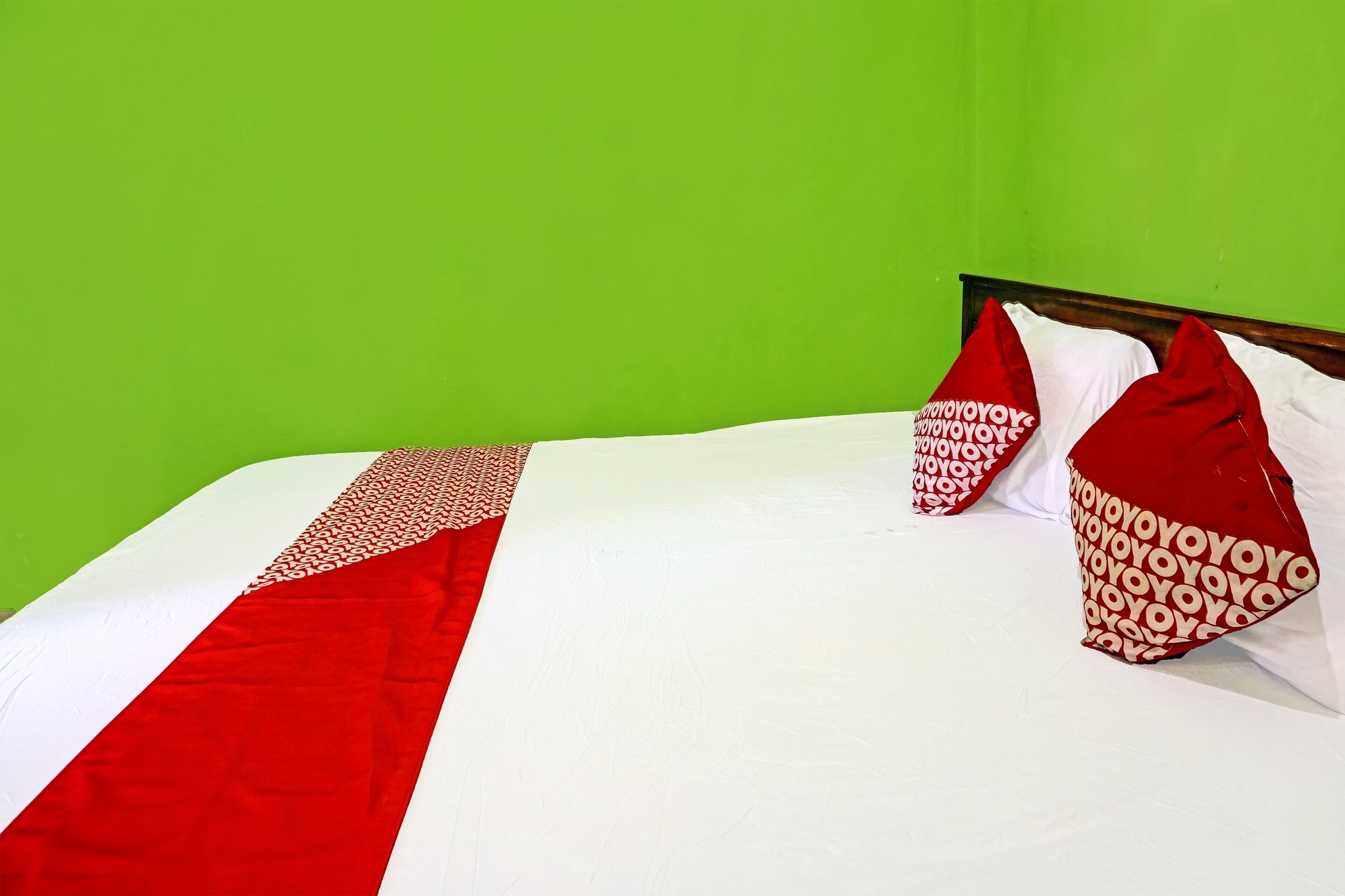 Ein Bett mit weißroter Bettdecke, zwei rote Kissen mit Muster und eine grüne Wand im Hintergrund.
