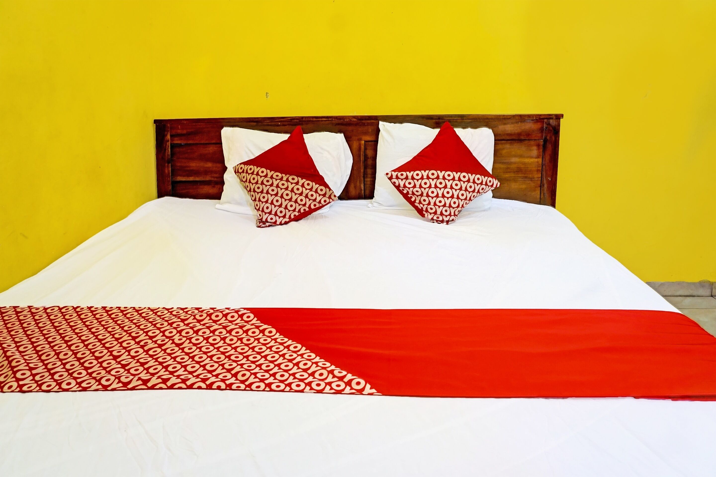 A bed with a wooden headboard, white bedding, and two red pillows with a circular pattern.