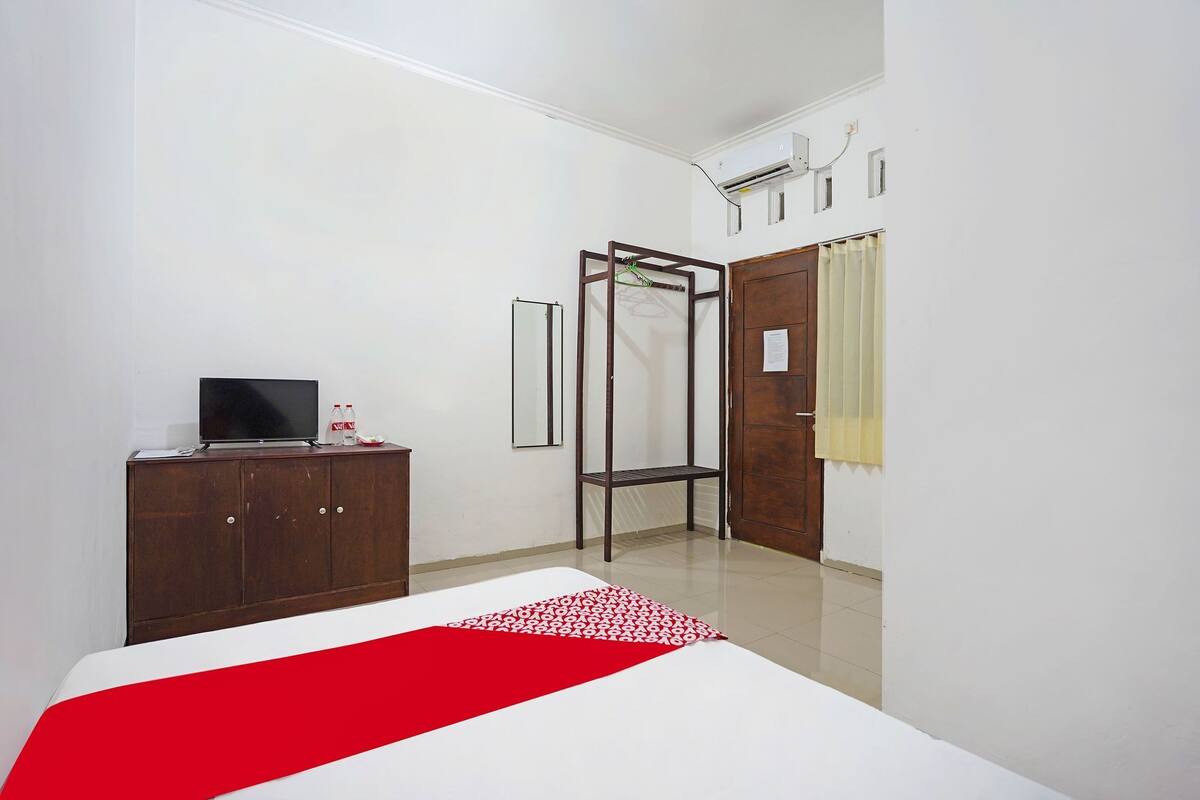 Een slaapkamer met een bed, een kledingkast, een televisie op een dressoir en een raam met gordijnen.