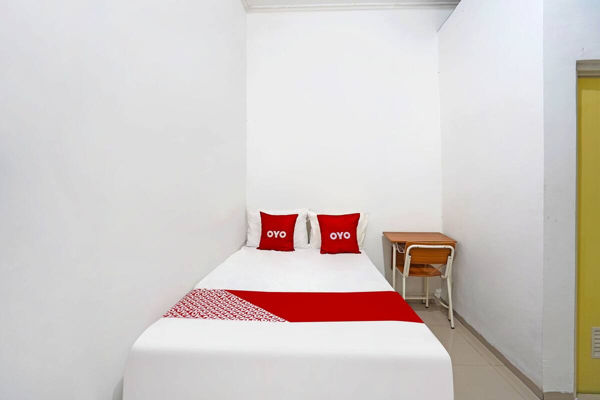 Een kleine, verzorgde slaapkamer met een enkel bed, twee kussens, een tafeltje en een stoel.