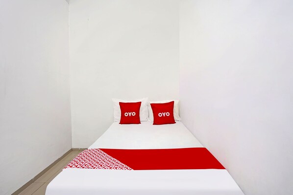 A small, single-bed room with white walls and a red and white patterned bedspread.