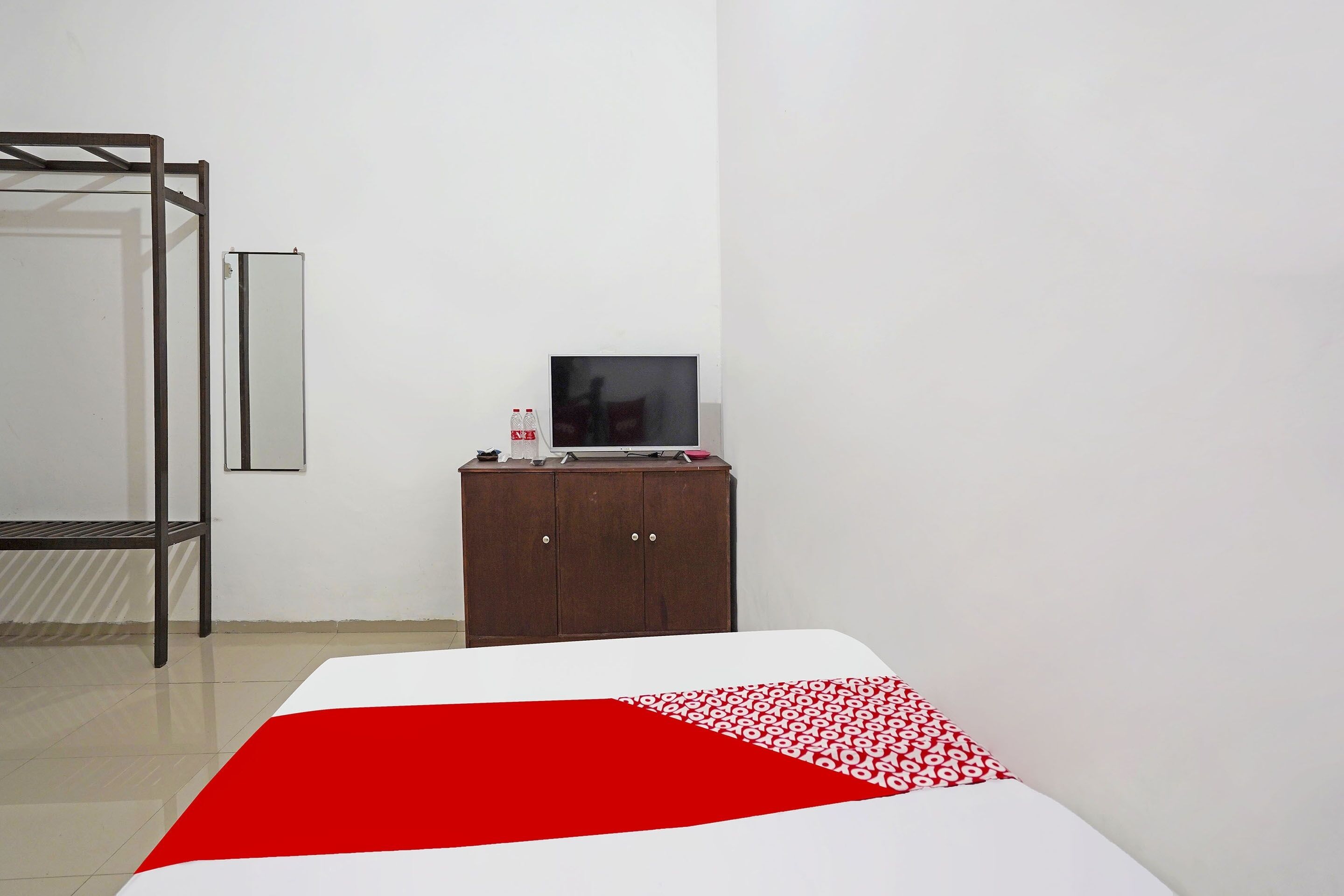 A hotel room with a bed, a wooden wardrobe, a desk with a computer, and a mirror on the wall.