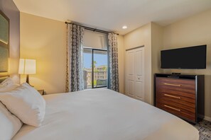 Habitación de hotel con una cama grande, un televisor de pantalla plana, un aparador y un balcón con cortinas.