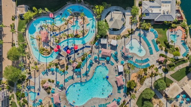 An aerial view of a resort with multiple swimming pools, sun loungers, and palm trees. - Coachella Shuttle, Lazy River: 3BR in Resort (Indio)
