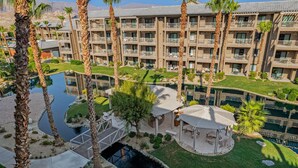 A hotel with multiple balconies, a swimming pool, and palm trees. - Coachella Shuttle, Lazy River: 3BR in Resort (Indio)