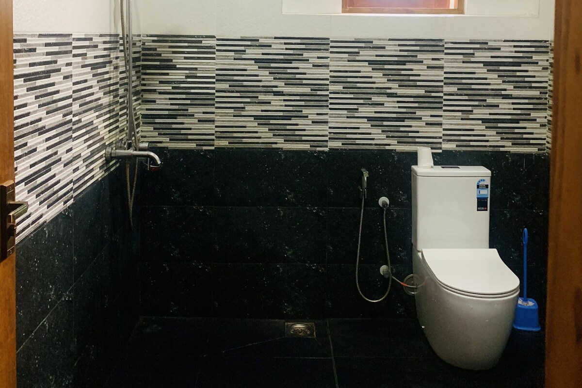 Et lille badeværelse med bruser, toilet og et vindue.