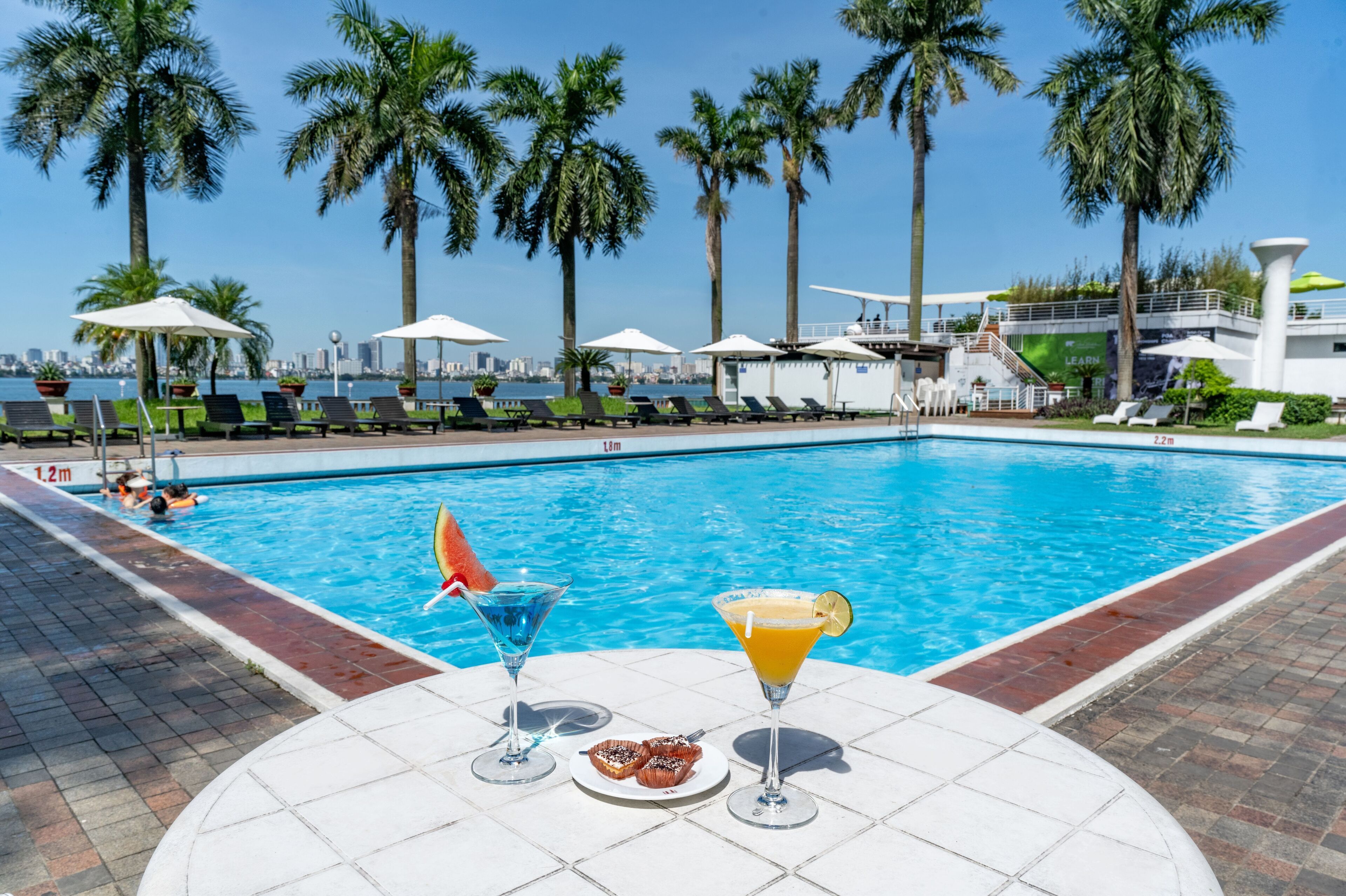 A poolside area with lounge chairs, umbrellas, and a view of the city skyline.