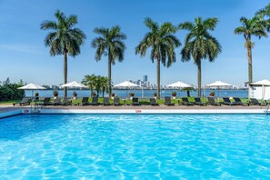 A swimming pool with lounge chairs and umbrellas, palm trees, and a city skyline in the background. -  Thang Loi Hotel Hanoi (Hanoi)