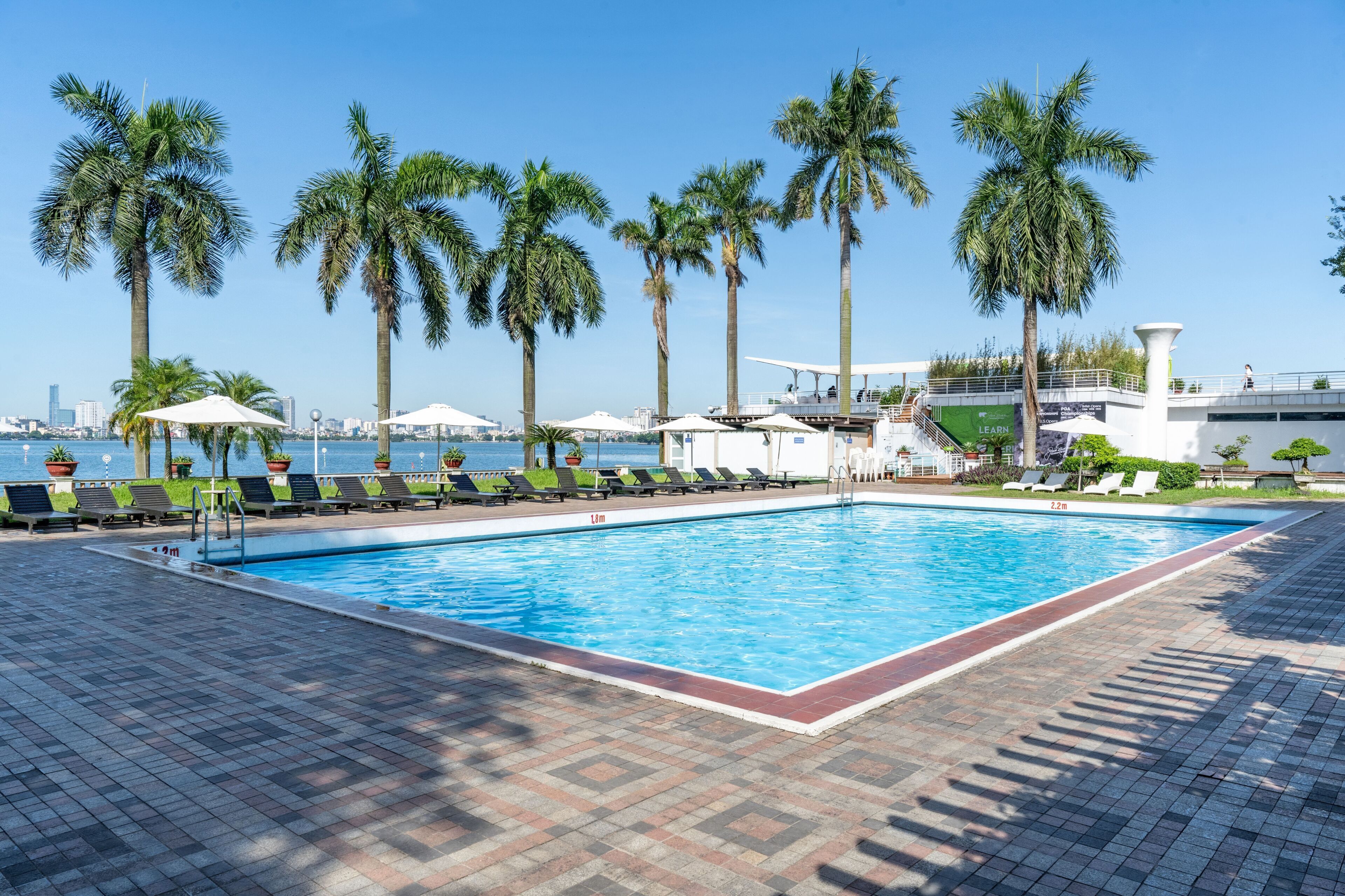 A swimming pool with lounge chairs and palm trees, surrounded by a tiled deck.