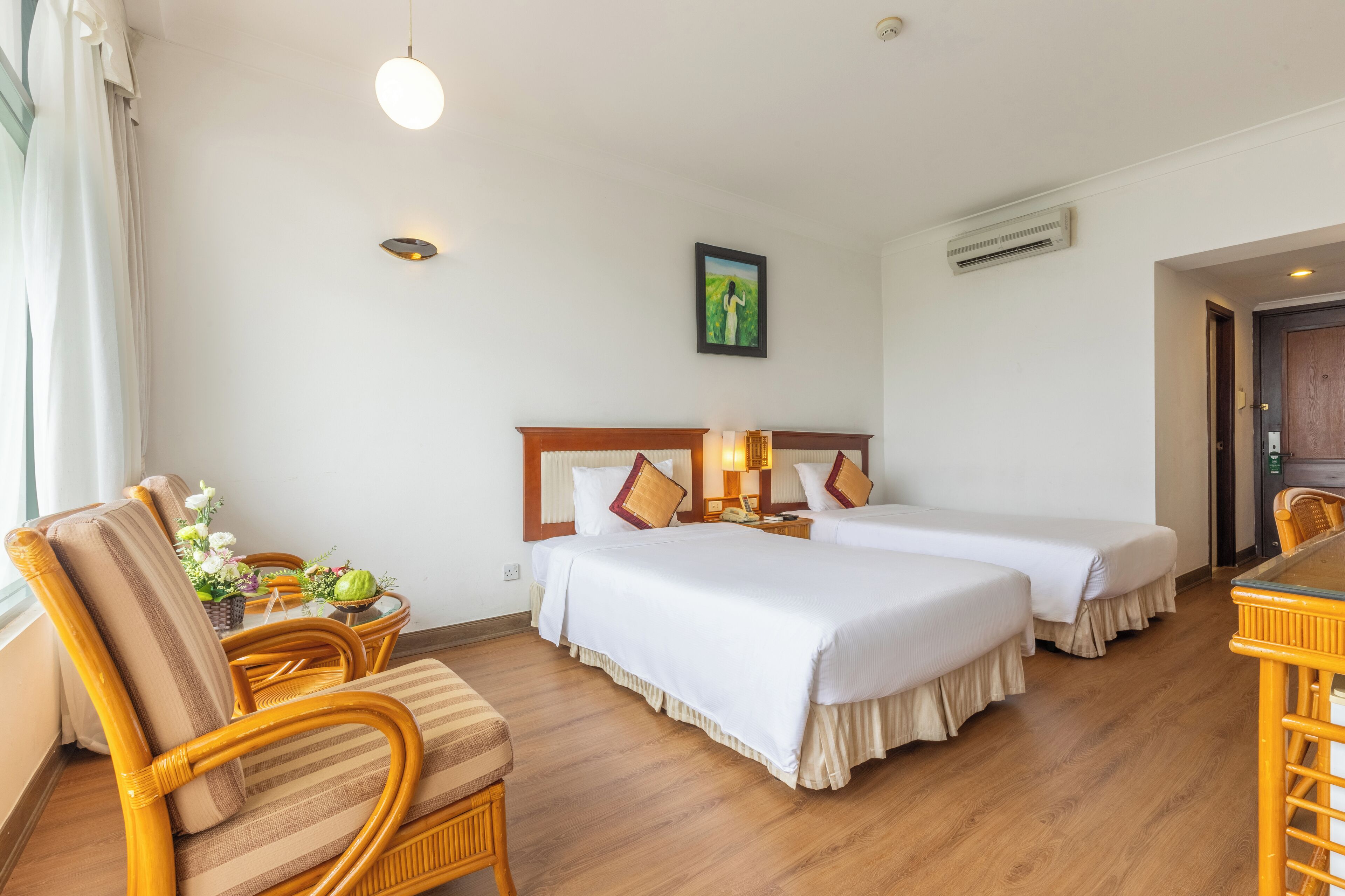 A hotel room with two beds, a sitting area with a chair and table, and a painting on the wall.