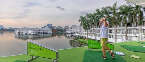 Campo de golf con un cuerpo de agua al fondo, palmeras y un paisaje urbano.