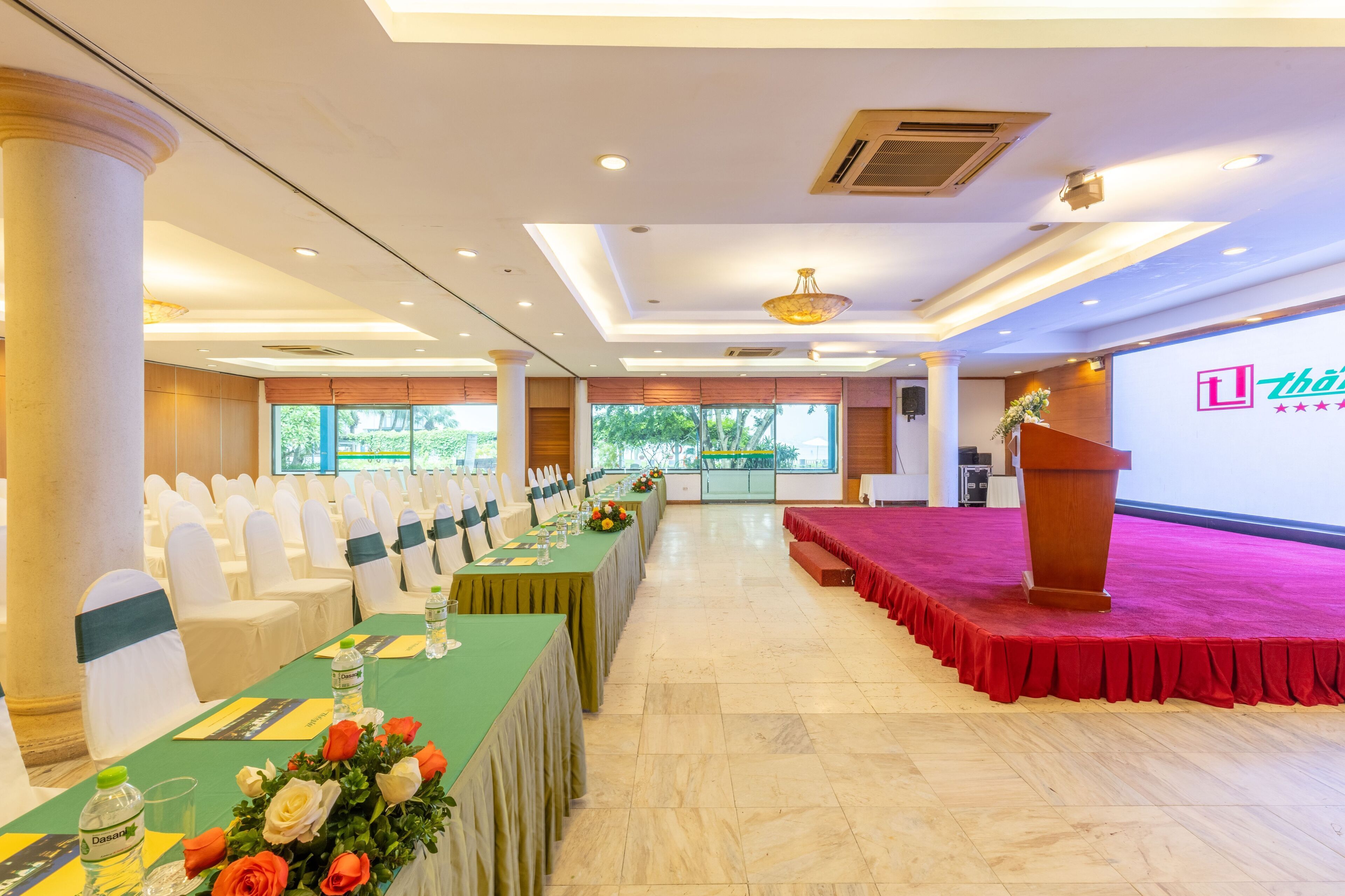 A conference room with rows of white chairs, a stage with a red carpet, and a podium.