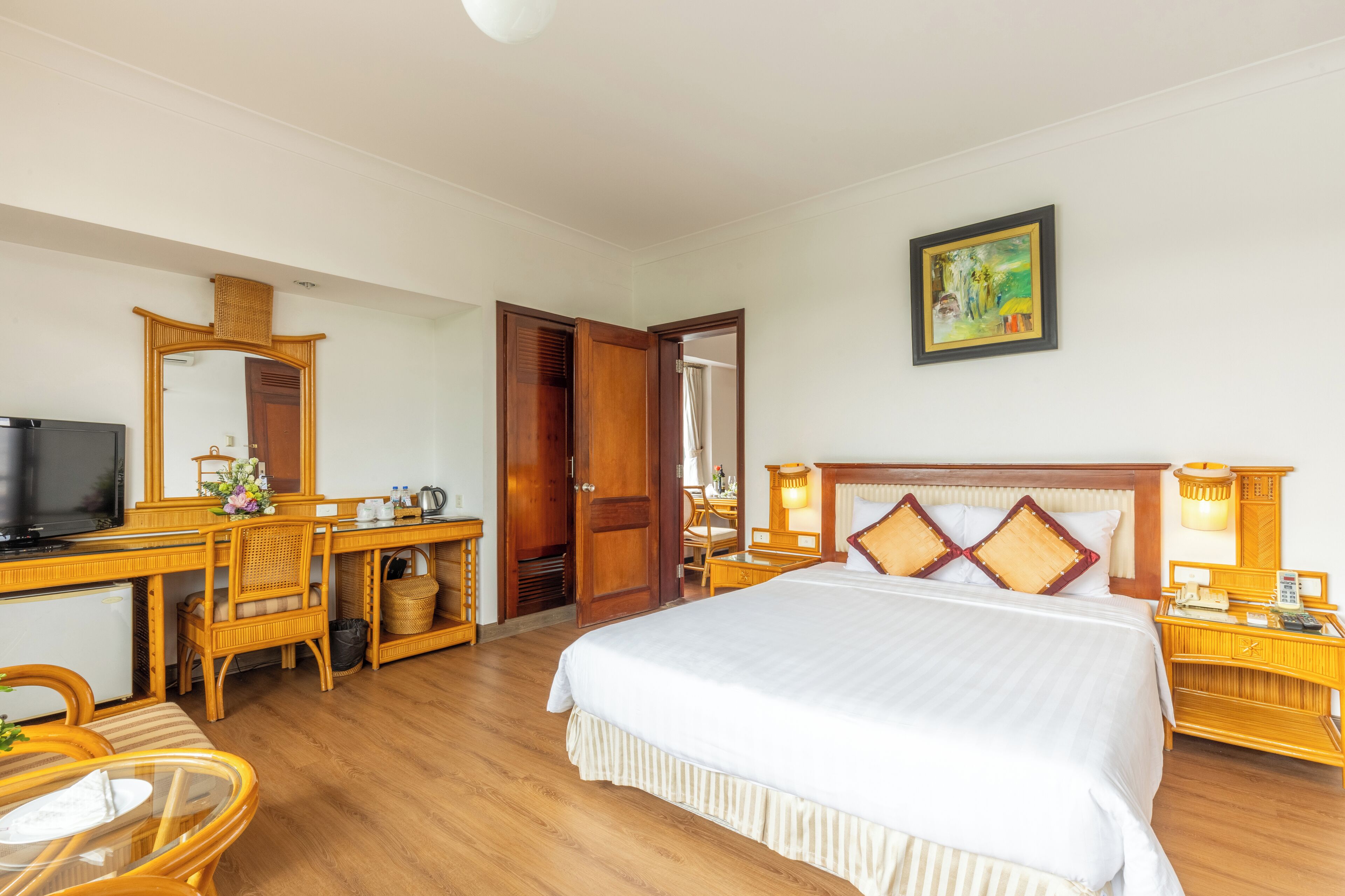 Een hotelkamer met een bed, een bureau met televisie, een stoel, een nachtkastje met lamp en een schilderij aan de muur.