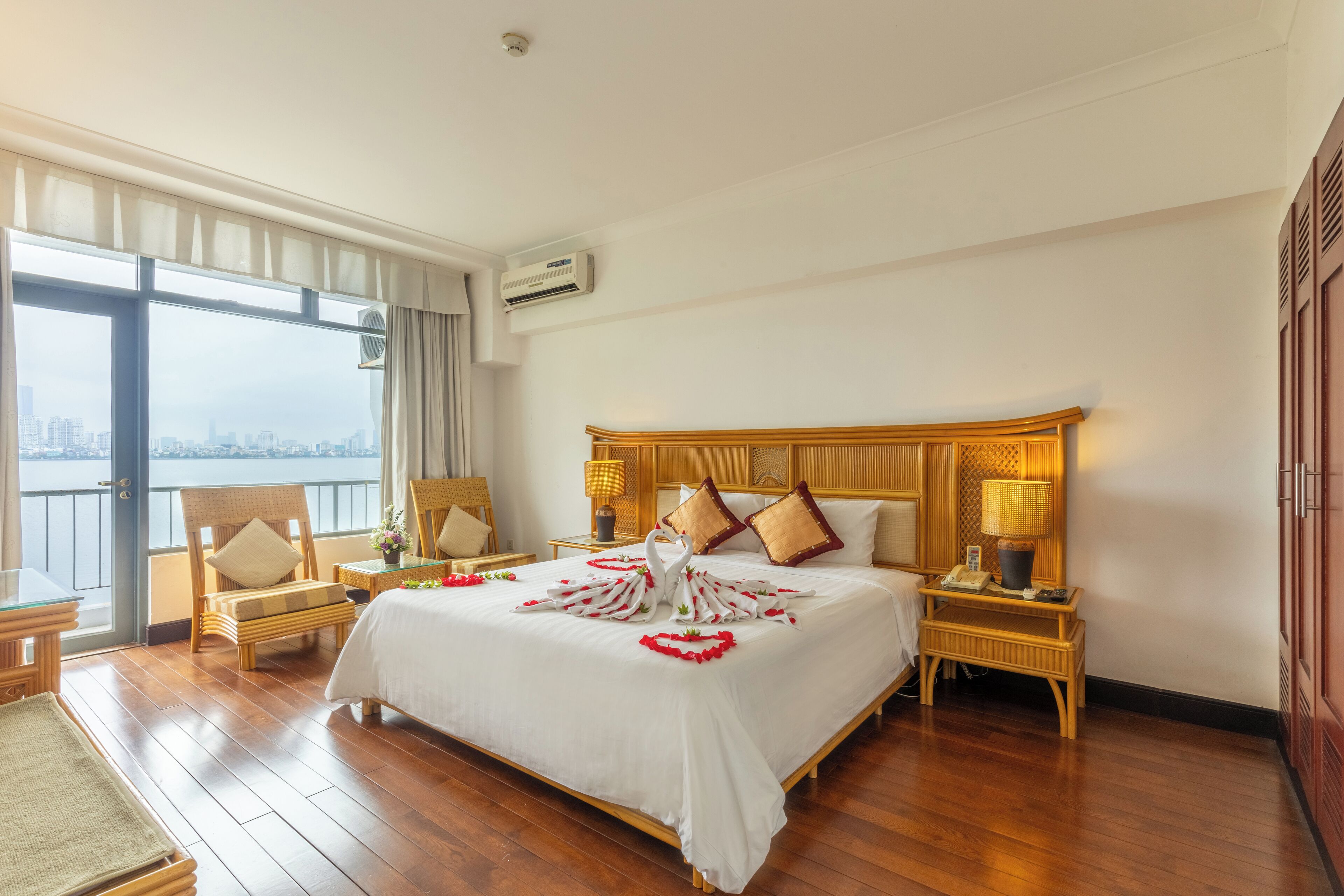 Habitación de hotel con una cama grande, dos mesitas de noche, una silla, una ventana con vistas a la ciudad y un equipo de aire acondicionado.