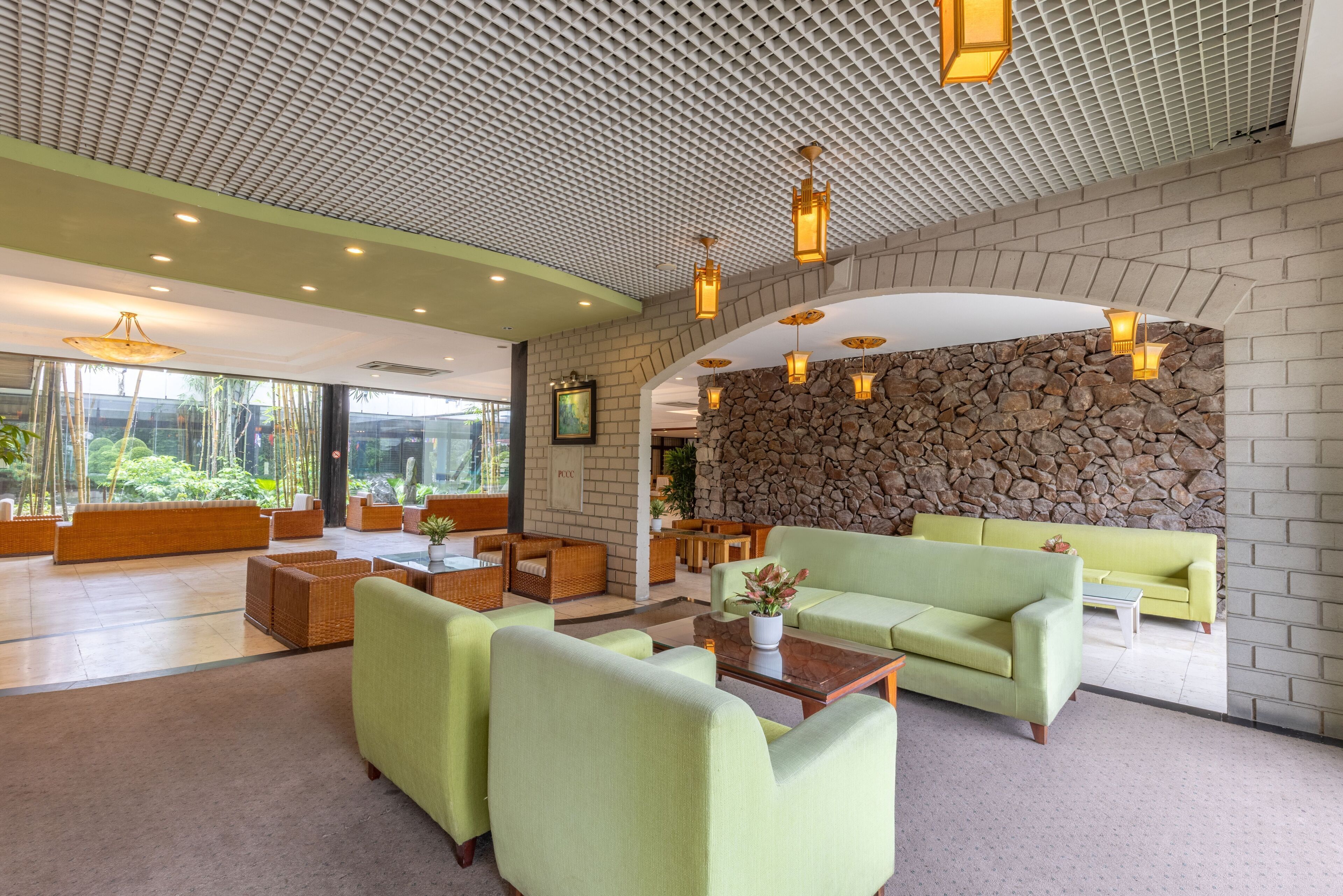 A spacious lobby with green sofas, wicker furniture, and a stone wall.